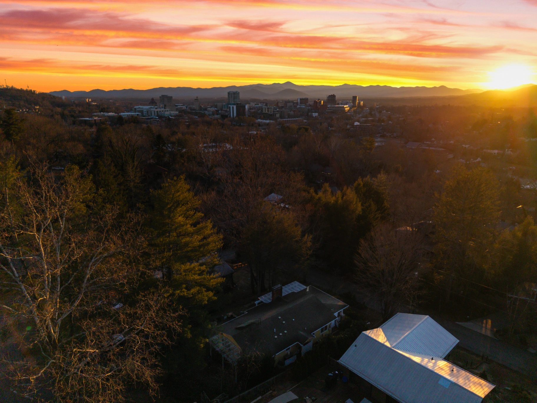 Aerial view of Asheville NC city skyline at sunset with Blue Ridge Mountain range — walkable vacation rental location