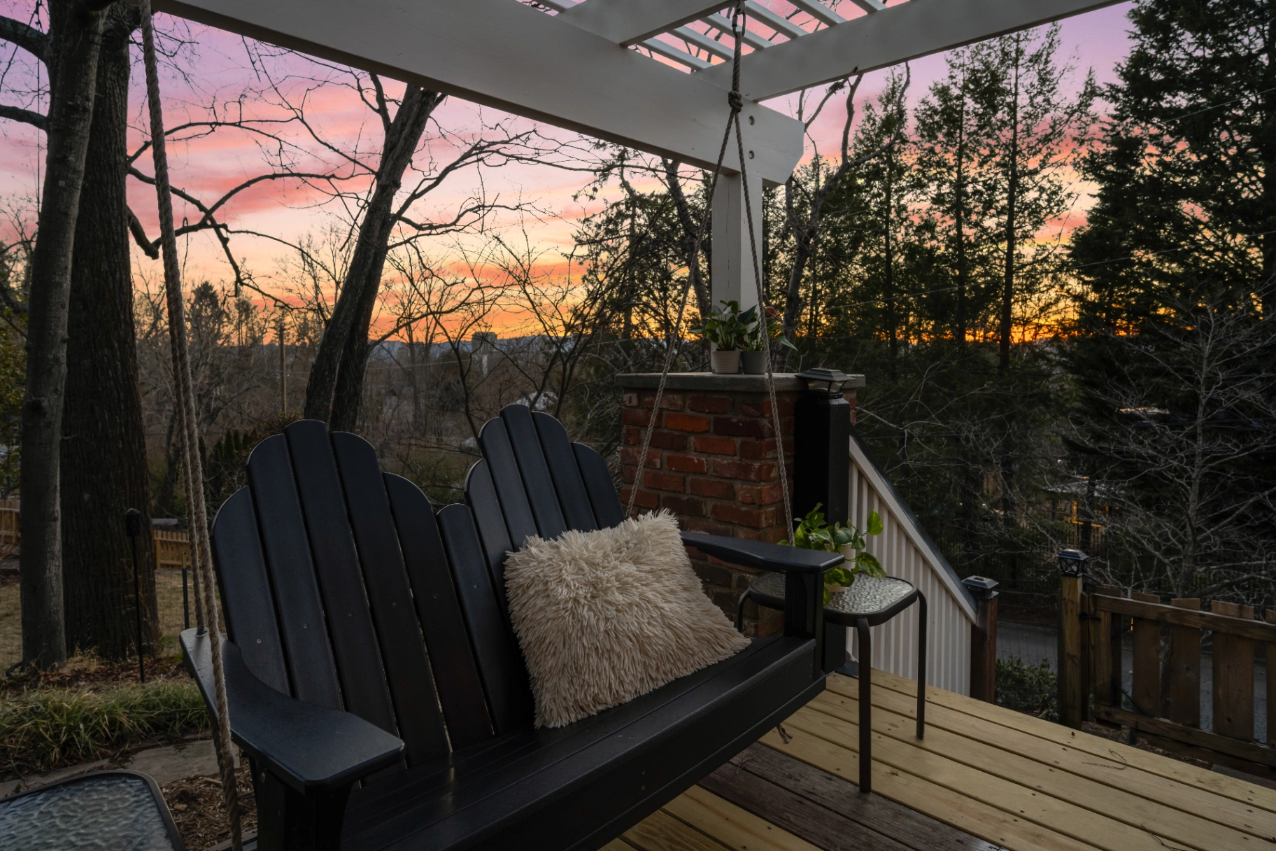 Black adirondack porch swing on wooden deck at sunset — relaxing outdoor space at Asheville rental