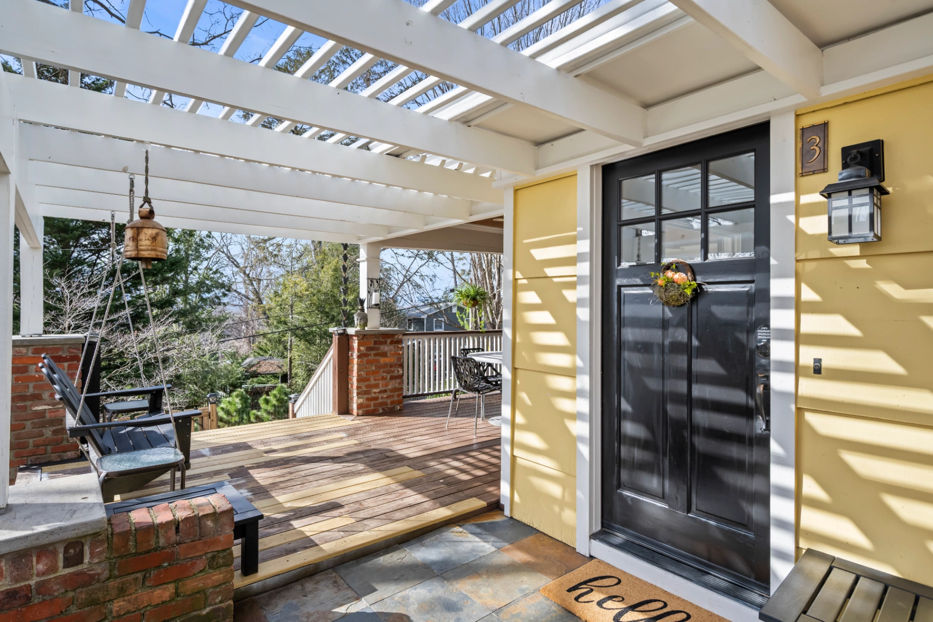 Exterior entrance of Asheville Intimate Gatherings — black front door, yellow siding, and white pergola, mid-century modern renovation