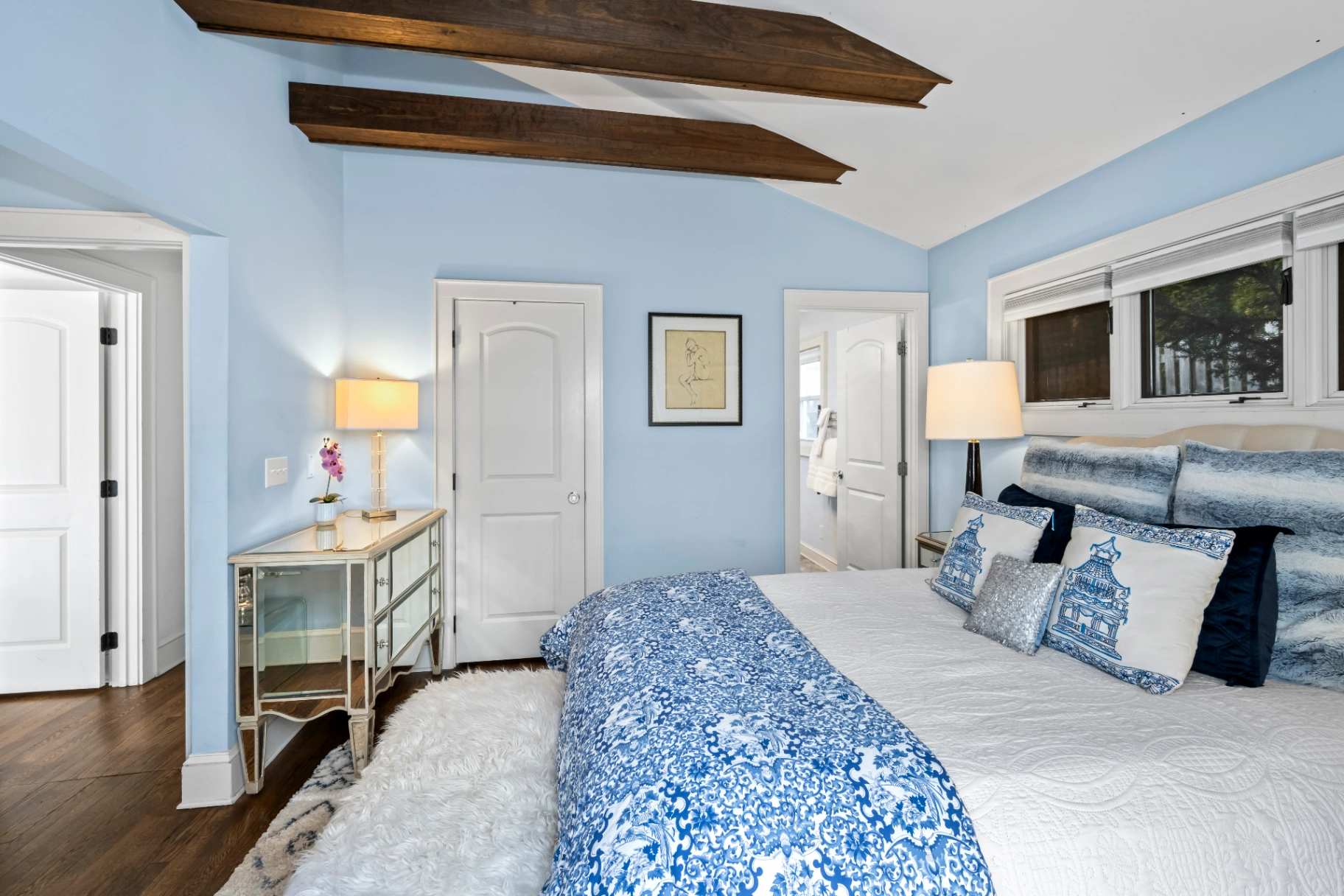Light blue bedroom with exposed ceiling beams and mirrored dresser — mid-century Asheville rental