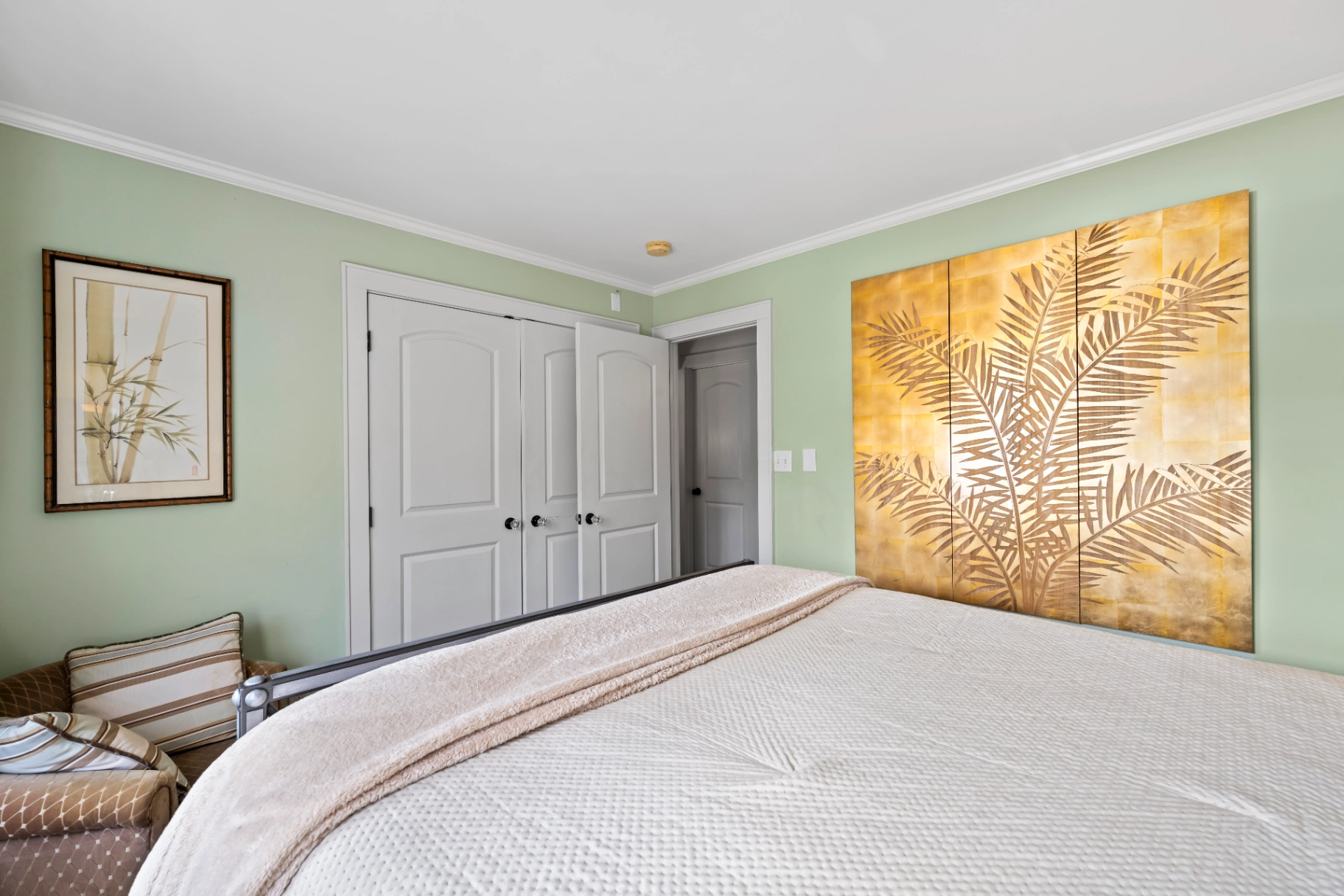 Light green bedroom with gold palm leaf artwork and white closet doors — Asheville vacation rental