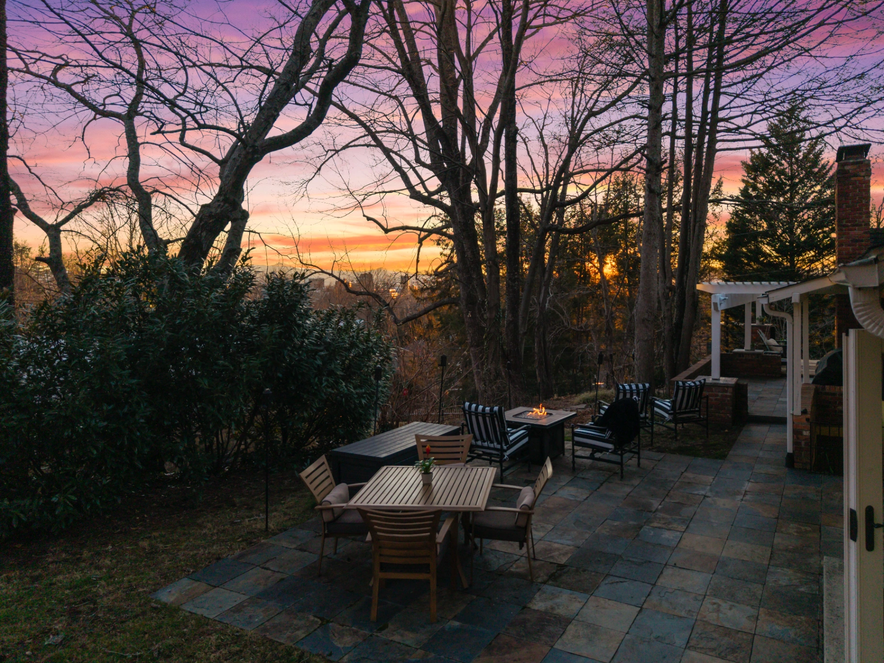 Outdoor stone patio with fire pit, dining area, and mountain sunset view — Asheville NC rental